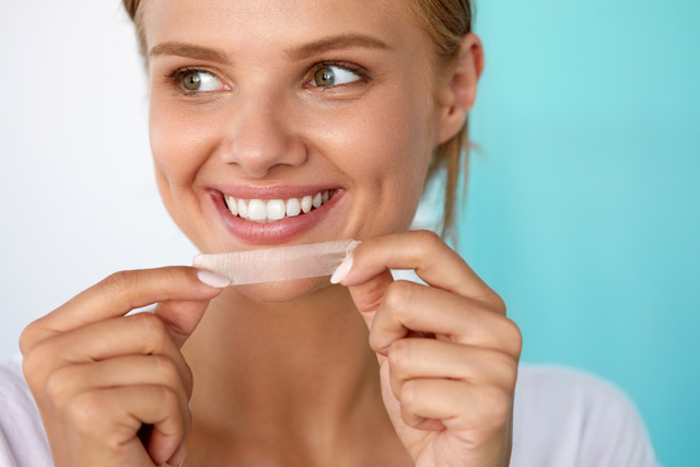 a woman smiling while holding a teeth whitening strip up to her face